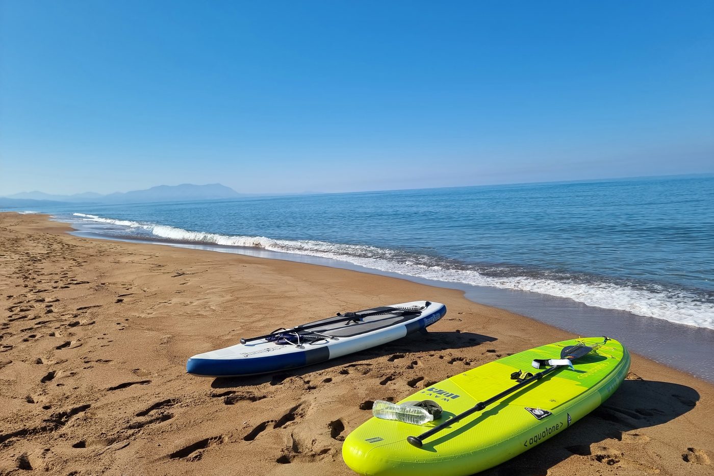 The sandy beach at Kato Samiko, with paddleboards resting on the sand and mountains along the horizon.