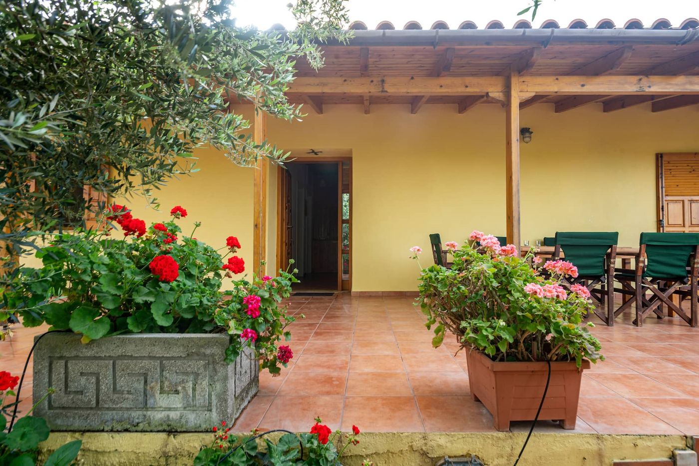 Green canvas chairs and pots of geraniums on the tiled veranda.